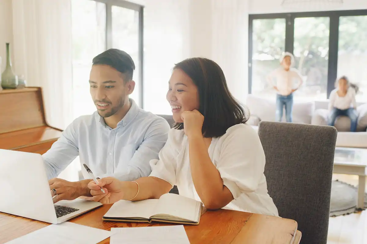 Couple reviewing documents and a laptop at home with children in the background